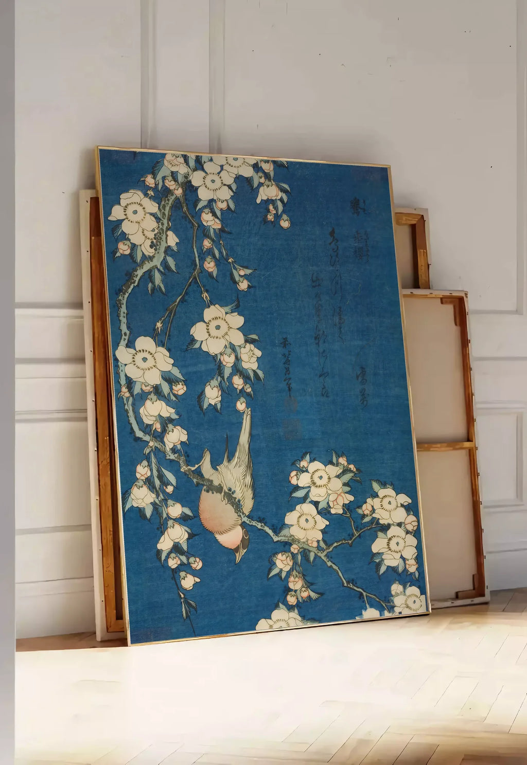 Tirage encadrable affiche Hokusai bouvreuil sur cerisier, posee au sol dans une entree lumineuse, contre un mur a panneaux blancs, a cote de chassis en bois empiles