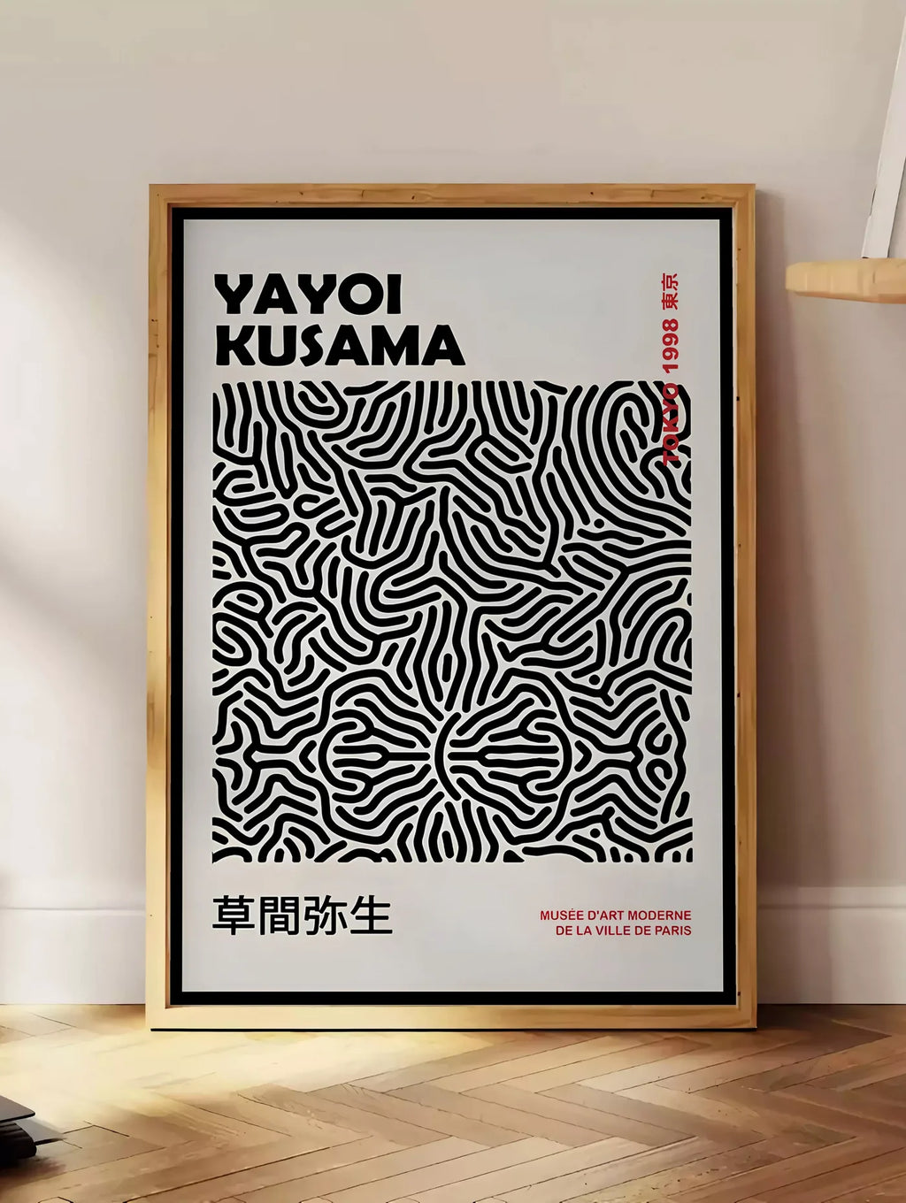 Estampe affiche filet infini de Kusama art japonais, posee au sol dans un coin salon, sur un parquet a chevrons, pres d'une table d'appoint en chene chargee de livres