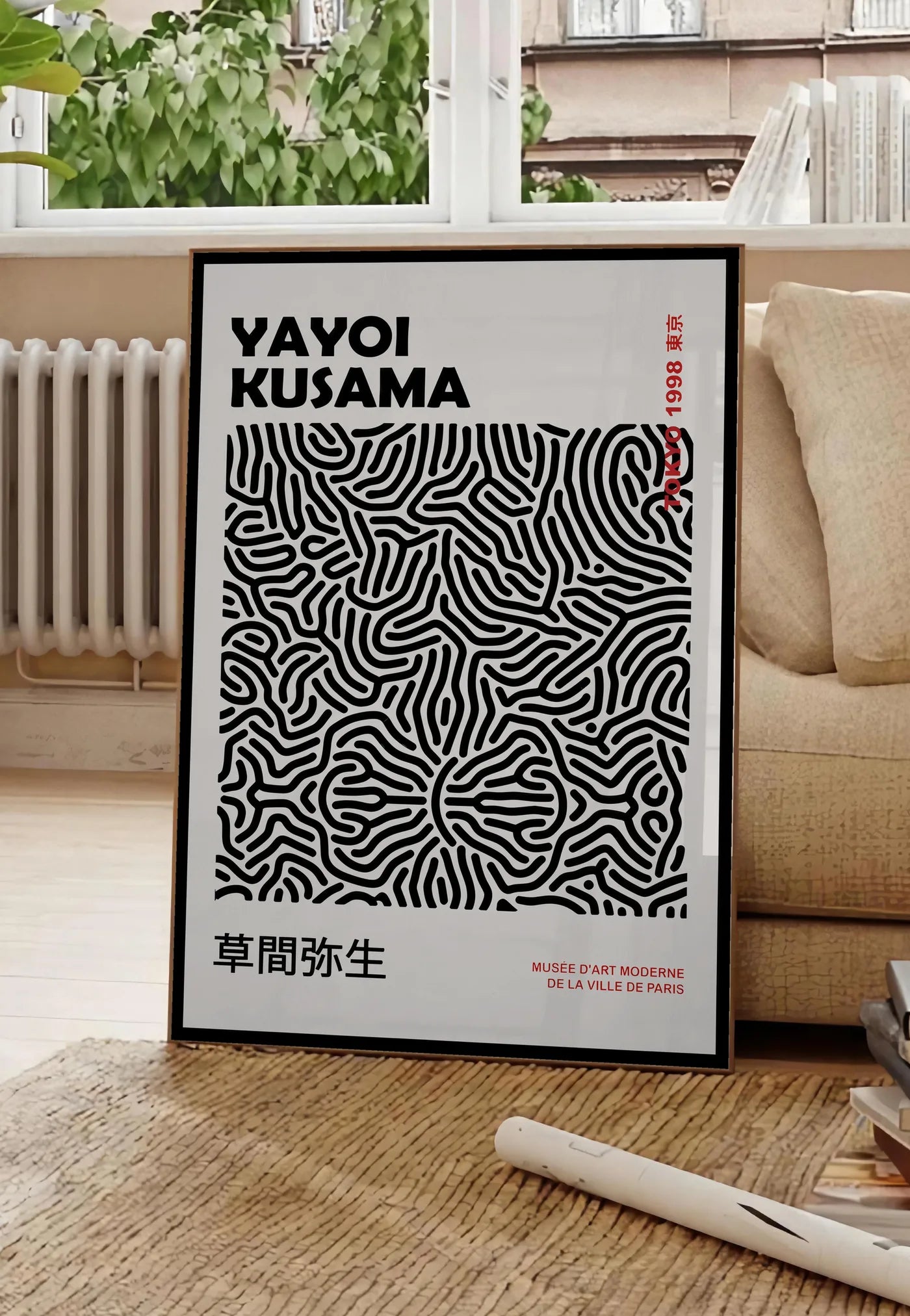 Poster affiche filet infini noir de Kusama art japonais, posee au sol dans un salon parisien, devant une grande fenetre donnant sur un immeuble haussmannien, entre un ficus et un canape creme