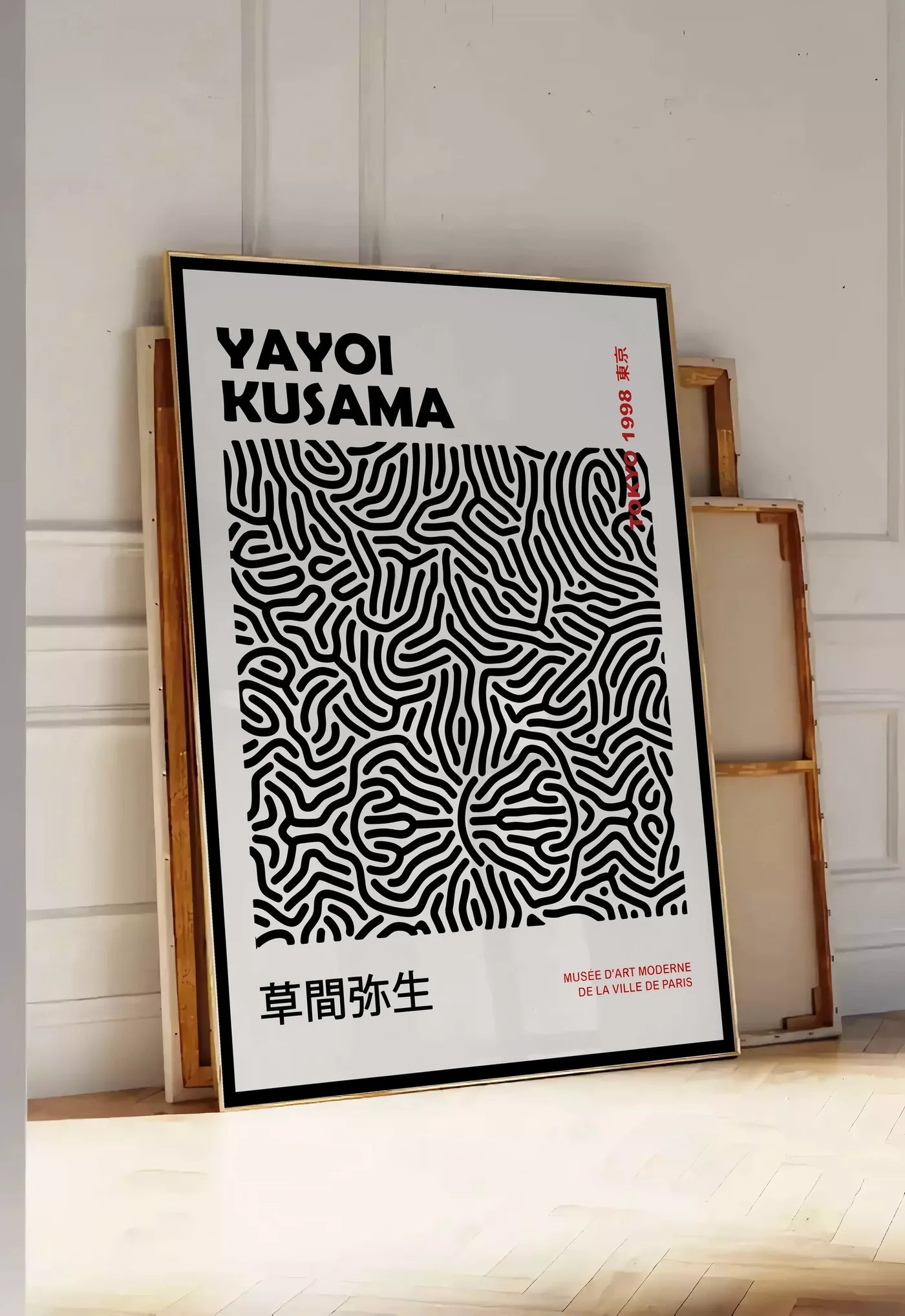 Tirage encadrable affiche filet infini noir de Kusama art japonais, posee au sol dans une entree lumineuse, contre un mur a panneaux blancs, a cote de chassis en bois empiles