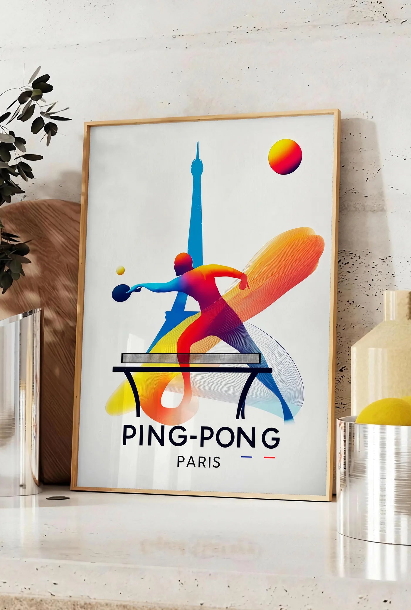 Affiche joueur de ping-pong dynamique a la raquette, posee sur un plan de travail de cuisine en pierre claire, entre une branche d'eucalyptus en vase et un bocal de citrons