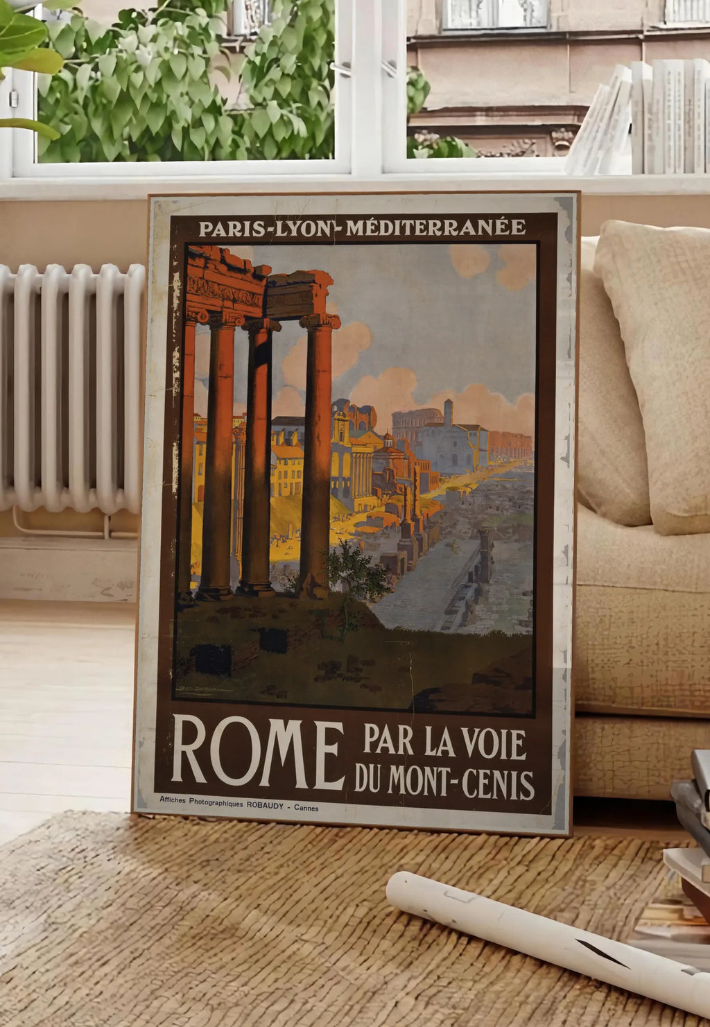 Poster affiche Rome vintage, posee au sol dans un salon parisien, devant une grande fenetre donnant sur un immeuble haussmannien, entre un ficus et un canape creme