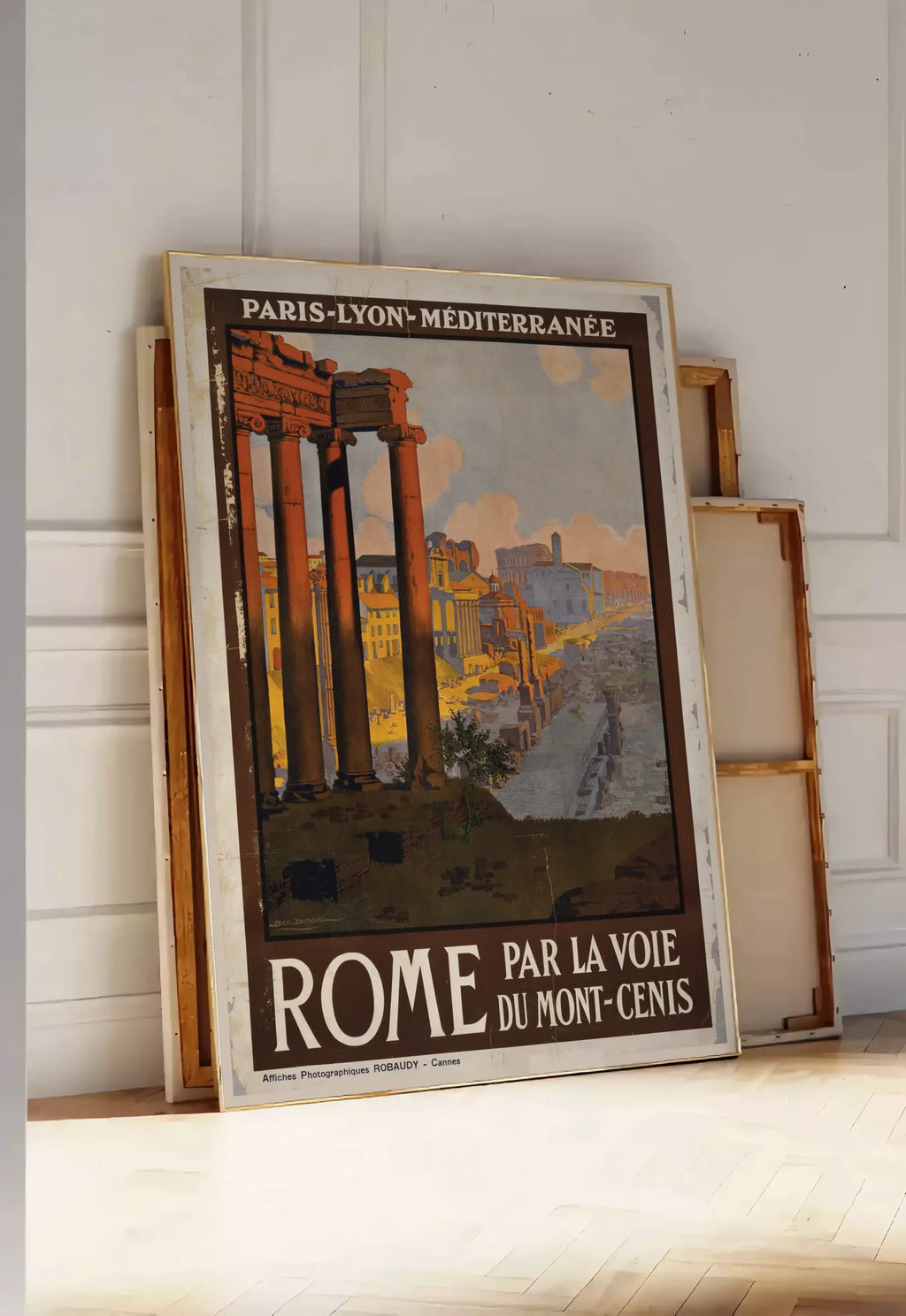 Tirage encadrable affiche Rome vintage PLM, posee au sol dans une entree lumineuse, contre un mur a panneaux blancs, a cote de chassis en bois empiles